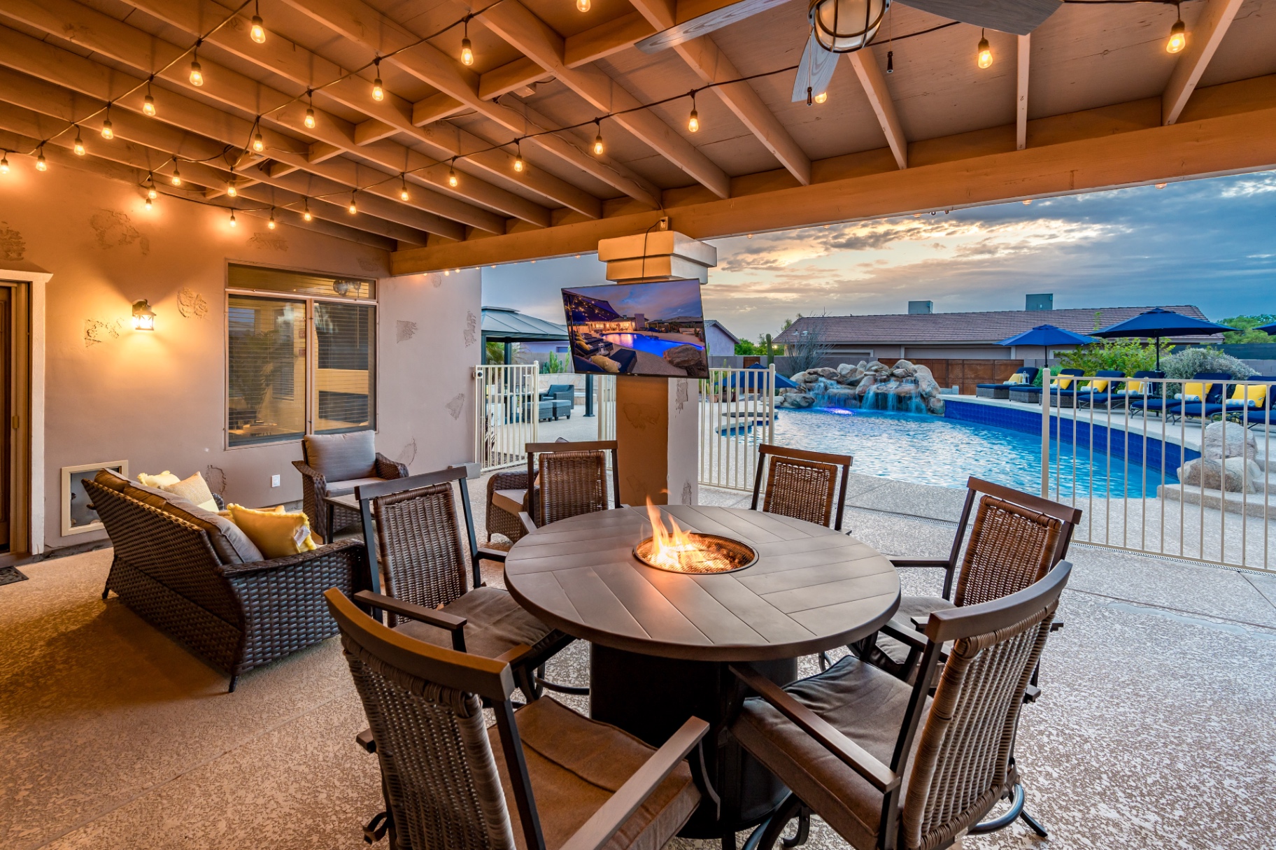 Covered patio fire pit table at sunset with TV and pool views