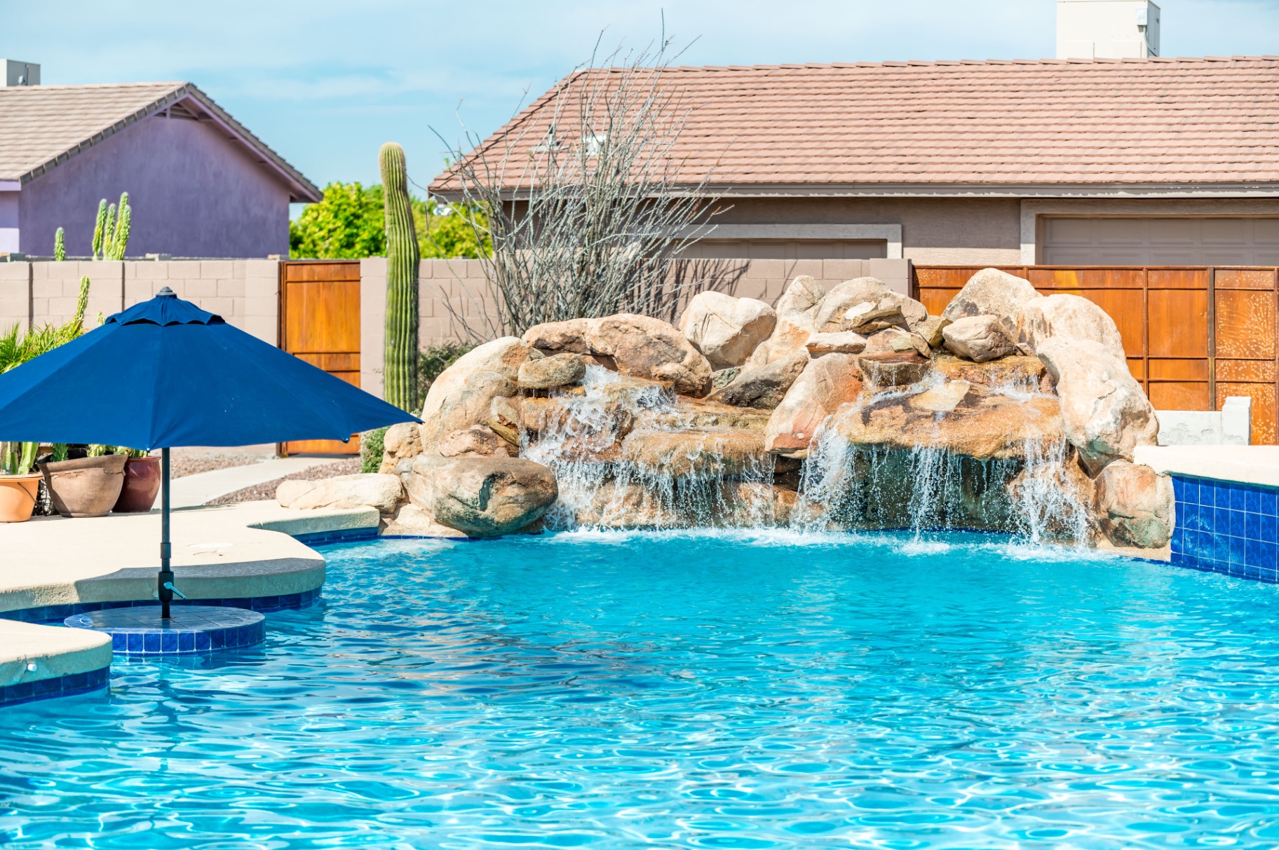Backyard pool with rock grotto waterfall and blue umbrella