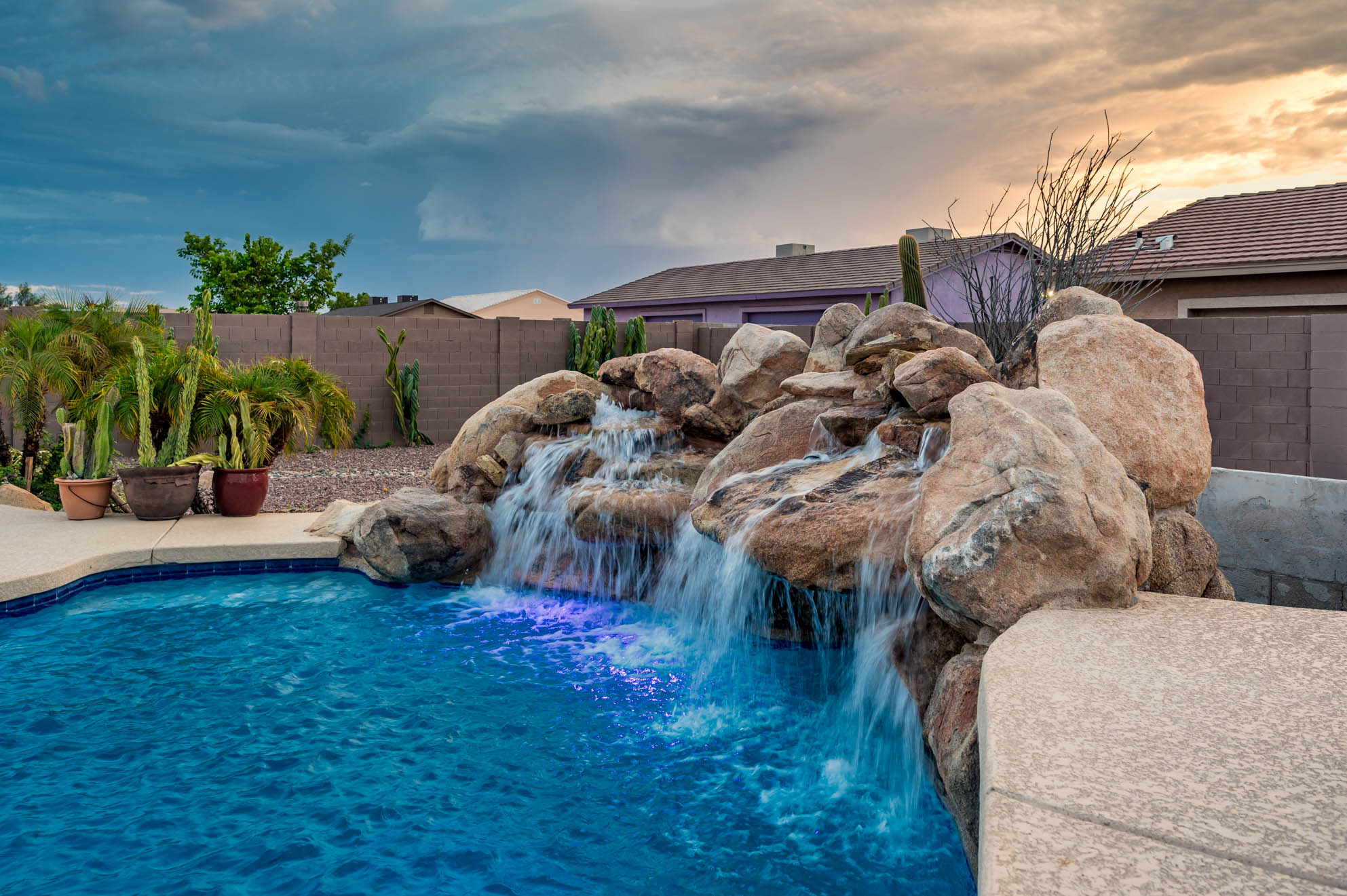 Heated diving pool with grotto waterfalls glowing at sunset at our Peoria, AZ vacation rental